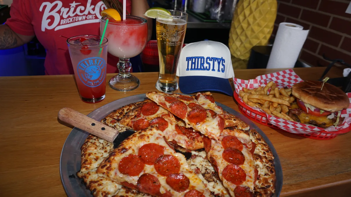 Two pepperoni pizzas, drinks and Thirsty's caps on the table